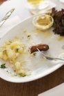 Salchichas sobrantes en ensalada de patata en plato blanco con tenedor - foto de stock