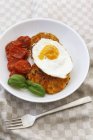 Carrot fritter with a fried egg and braised tomatoes on white plate over towel with fork — Stock Photo