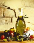 Uma garrafa de azeite com azeitonas e tomates contra a parede de tijolo — Fotografia de Stock