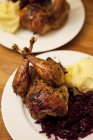 Жареный фазан с красной капустой и картофельным пюре на белой тарелке на деревянной поверхности — стоковое фото