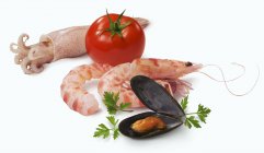 An arrangement of seafood and a tomato  on white surface — Stock Photo
