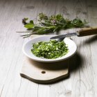 Elevated view of fresh chopped herbs in bowl on wooden board — Stock Photo