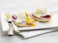 Яйца Бенедикт с вилкой и ножом на белой тарелке — стоковое фото