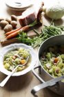 Minestra di verdure con ingredienti su piatto con cucchiaio in pentola sopra tavolo di legno — Foto stock