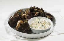 Artichokes with a garlic dip  on white plate over towel — Stock Photo