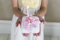 Closeup view of girl holding a cake with lit candle and Happy birthday tag — Stock Photo