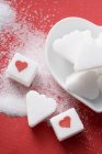 Terrones de azúcar en forma de corazón con corazones rojos en la superficie roja - foto de stock