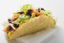 Taco filled with sweetcorn and beans on paper napkin on white surface — Stock Photo