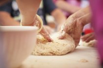 Massa de pão sendo amassada por mãos ove superfície de madeira — Fotografia de Stock