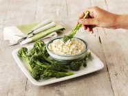 Broccoli with a dip  on white plate over wooden surface — Stock Photo