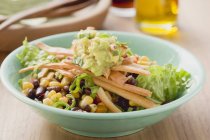 Closeup view of lettuce with beans, sweetcorn, Tortilla strips and guacamole in green bowl — Stock Photo