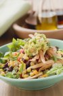 Salat, Bohnen, Mais, Tortilla-Streifen und Guacamole auf grünem Teller über Holzoberfläche — Stockfoto