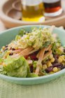 Salat, Bohnen, Mais, Tortilla-Streifen und Guacamole auf grünem Teller — Stockfoto