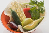 Крупный план кукурузного початка с авокадо, перцем, травой, луком и лаймом в миске — стоковое фото