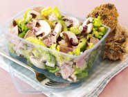Mixed leaf salad with sausages, mushrooms and avocados in a plastic container — Stock Photo