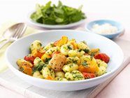 Gnocchi with oven-roasted vegetables and pesto on white plate  over wooden desk — Stock Photo