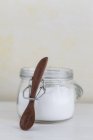 Closeup view of sugar in jar with wooden spoon on white surface — Stock Photo