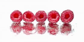 Fresh raspberries on wet mirror — Stock Photo