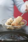 Woman taking deep-fried spring rolls out of wok — Stock Photo