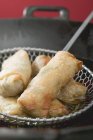 Closeup view of deep-fried spring rolls in a skimmer and wok — Stock Photo