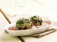 Spinach dumplings in tomato sauce on white plate over towel — Stock Photo