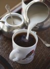 Derramando leite em xícara de café — Fotografia de Stock
