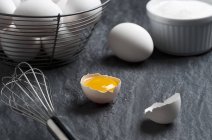Cracked egg with whisk and wire basket — Stock Photo