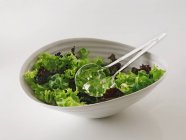 Mixed lettuce in bowl with salad servers — Stock Photo
