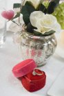 Vista close-up de flores em um vaso e anel de noivado na caixa em forma de coração vermelho — Fotografia de Stock