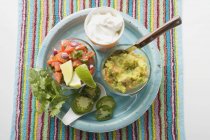 Guacamole, salsa and sour cream on plate over towel — Stock Photo