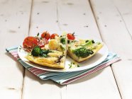 Картофельная лепешка с брокколи и помидорами на белой тарелке поверх полотенца — стоковое фото