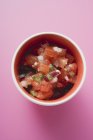Tomato salsa in a pot over pink surface — Stock Photo