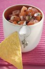 Tomato salsa in pot with spoon, nacho beside it — Stock Photo