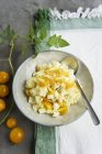 Kartoffelsalat mit gelben Tomaten auf weißem Teller mit Löffel über Handtuch — Stockfoto