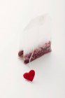 Vista de perto de um saco de chá com coração vermelho na superfície branca — Fotografia de Stock