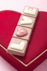 Closeup view of chocolate bar with love word on velvet heart-shape cushion — Stock Photo