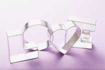 Closeup view of cookie cutters forming word Love on purple surface — Stock Photo