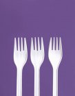 Primo piano vista di tre forchette di plastica bianca su uno sfondo viola — Foto stock