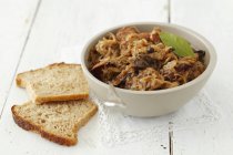 Bigos - sauerkraut with sausage and bacon in white bowl on wooden surface — Stock Photo