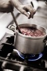 A cook seasoning tomato sauce with salt at saucepan on cooker — Stock Photo