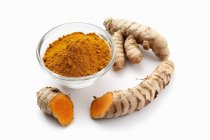 Turmeric powder in bowl and roots — Stock Photo