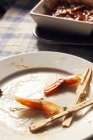 Вид крупным планом на хвост креветок остается с зубочистками на грязной тарелке — стоковое фото