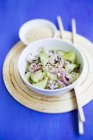 Cucumber salad with red onions and sesame seeds on white plate over blue surface — Stock Photo