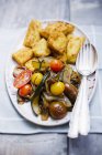 Zucchini mit Polentastücken und Tomaten auf weißem Teller mit Gabel und Löffel über dem Tisch — Stockfoto