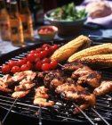 Chicken wings, prawn skewers, baby sweetcorn and tomatoes on the barbecue grill — Stock Photo