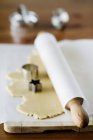 Elevated view of rolled-out biscuit dough with rolling pin in paper and cookie cutters — Stock Photo