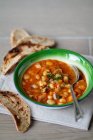 Bean and chickpea stew with toasted bread on green plate with spoon — Stock Photo