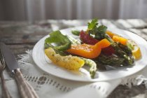Vegetable salad with asparagus and peppers on white plate over towel — Stock Photo