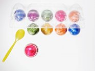 Vista superior de ovos coloridos em uma xícara de ovo e em uma caixa de ovo transparente — Fotografia de Stock