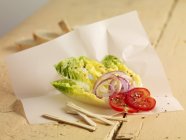 Листя салату з цибулею і помідорами на папері над дерев'яною поверхнею — стокове фото